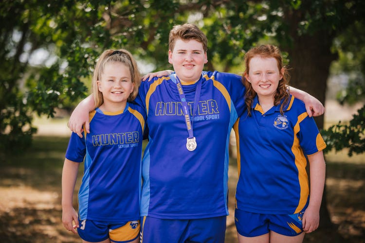 three students wearing their sports representative uniforms with medals
