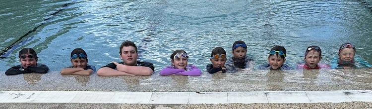 Children in the pool in a line facing over the edge